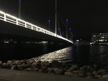 Upplyst bro över ett vatten, ljuset speglar sig i vattnet.
