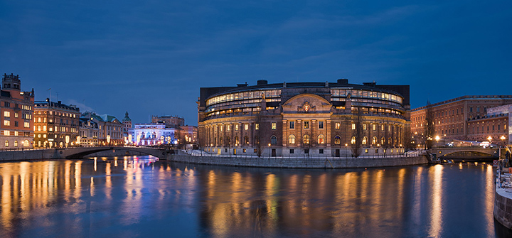 kvällsbild fårn stockholm, stora byggnader med ljus som speglar sig i vattnet. Foto.