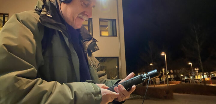 En man med pannlampa och en fladdermusdetektor, står på en gata på kvällen. Foto.