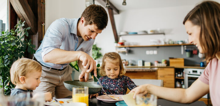 Father of a young family is putting eggs on a daughters plate for a breakfast. Foto.