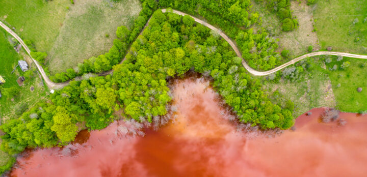 Flygfoto över en spillvatten från en koppargruva. Aerial view of colorful red copper mining waste water in contrast with fresh green forest by drone. Foto.