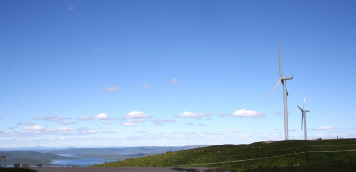 Ett par vindkraftverk på en höjd, vy över vidsträckt landskap.