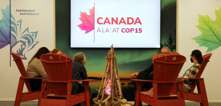 En sittgrupp kring en uppbygd fejk-eldstad under en skylt där det står Canada á la, at COP 15. Foto.