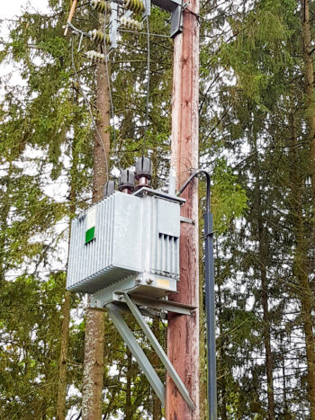 ledningsstolpar med transformatorstation som en grå låda. Åvanpå lådan är tre svarta plastkoner. Foto.