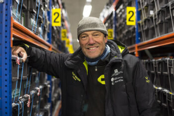 En person i vinterjacka mellan två rader av hyllplan. Foto.